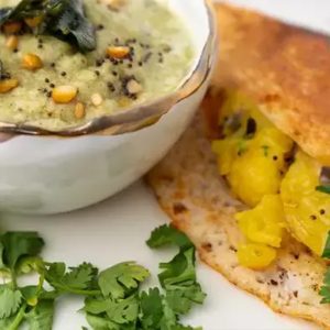 Masala-Dosa mit Curry-Kartoffelfüllung, angerichtet auf einem weißen Teller, dazu köstliches Kokosnuss-Chetney.