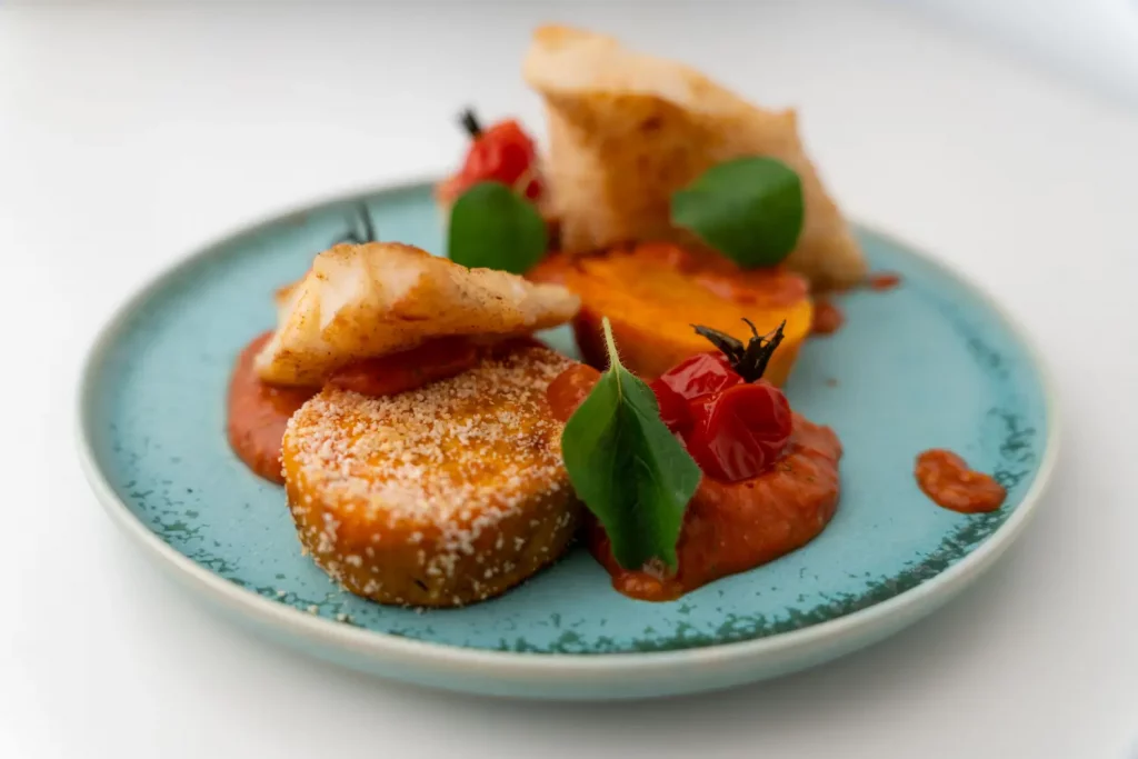Gebratener Kabeljau mit Süßkartoffel angerichtet auf einem blauen Teller mit Tomaten und Oregano-Blättern