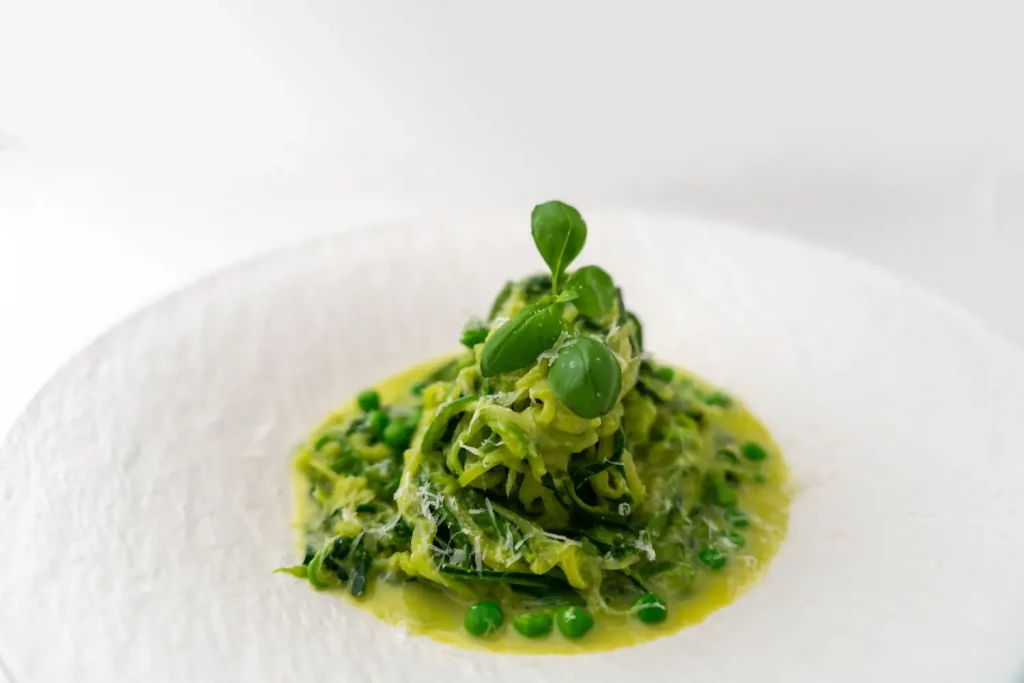 Zucchinispaghetti mit Erbsensauce angerichtet auf einem weißen Teller mit Basilikumblättern