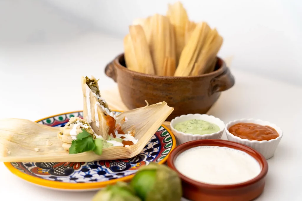 Mexikansiche Maistaschen mit Füllung angerichtet auf einem farbenfrohen Teller mit Koriander-Blättern. Daneben stehen drei verschiedenen Saucen.