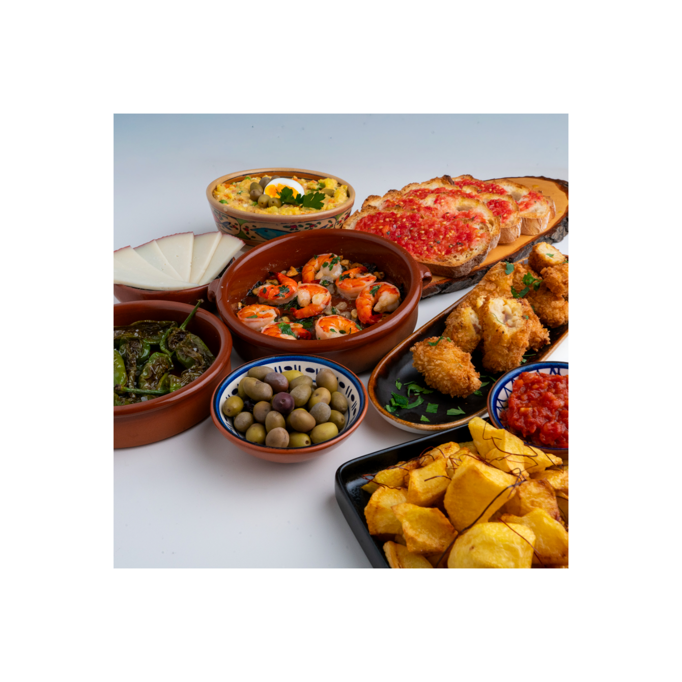 Spanische Tapas-Auswahl mit Garnelen, Patatas Bravas, Pimientos de Padrón, Tomatenbrot, Ensaladilla rusa, croquetas de jamon, Oliven und Manchego-Käse